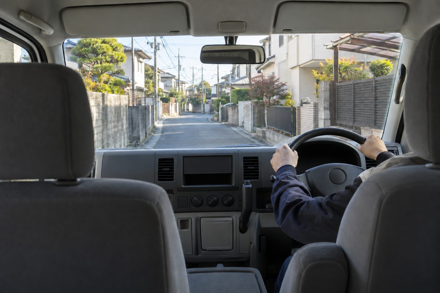 白いミニバンの後ろの席から見た、ハンドルを握る運転手の手元と、朝の住宅街の細い道